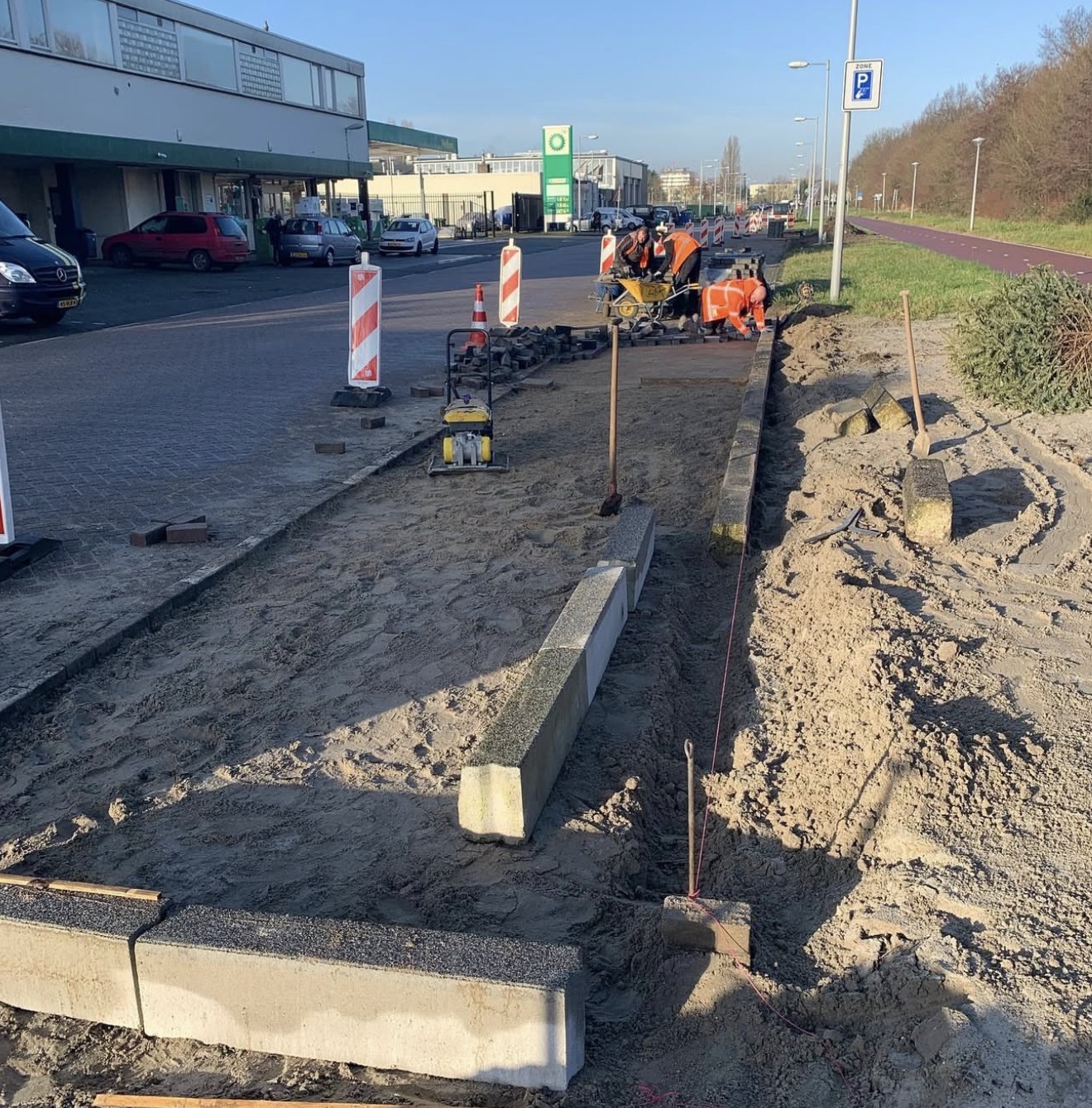 Stratenmakers in oranje werkkleding leggen bestrating langs een weg